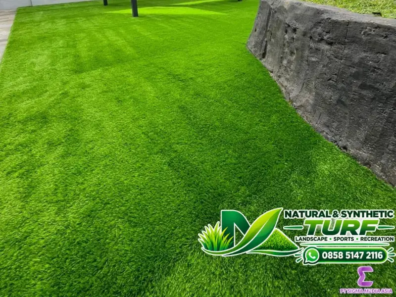 Halaman rumah berlapis rumput sintetis di samping dinding batu
