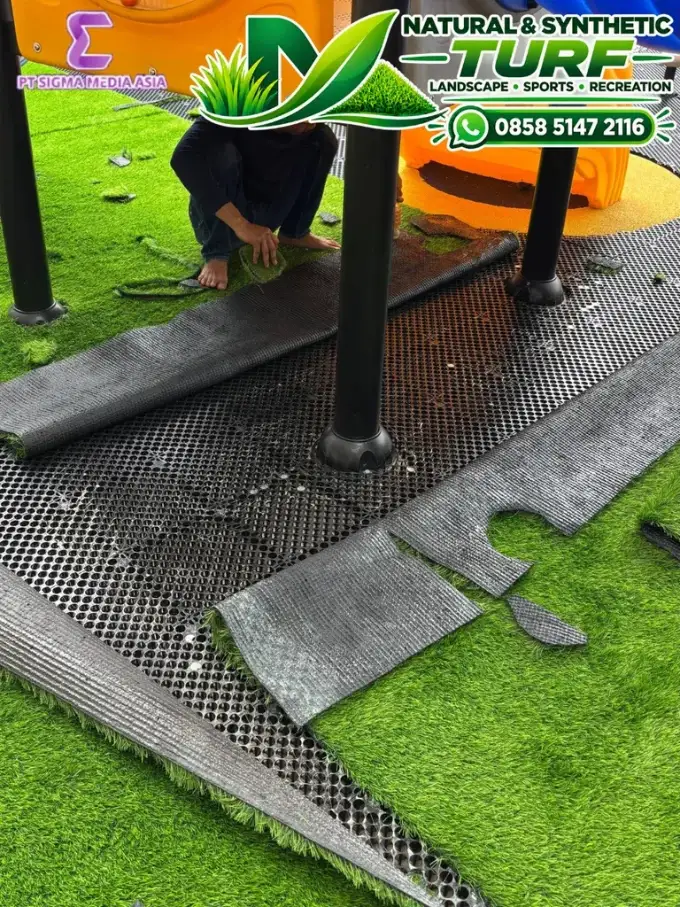 Tukang menggelar rumput sintetis di atas lapisan dasar