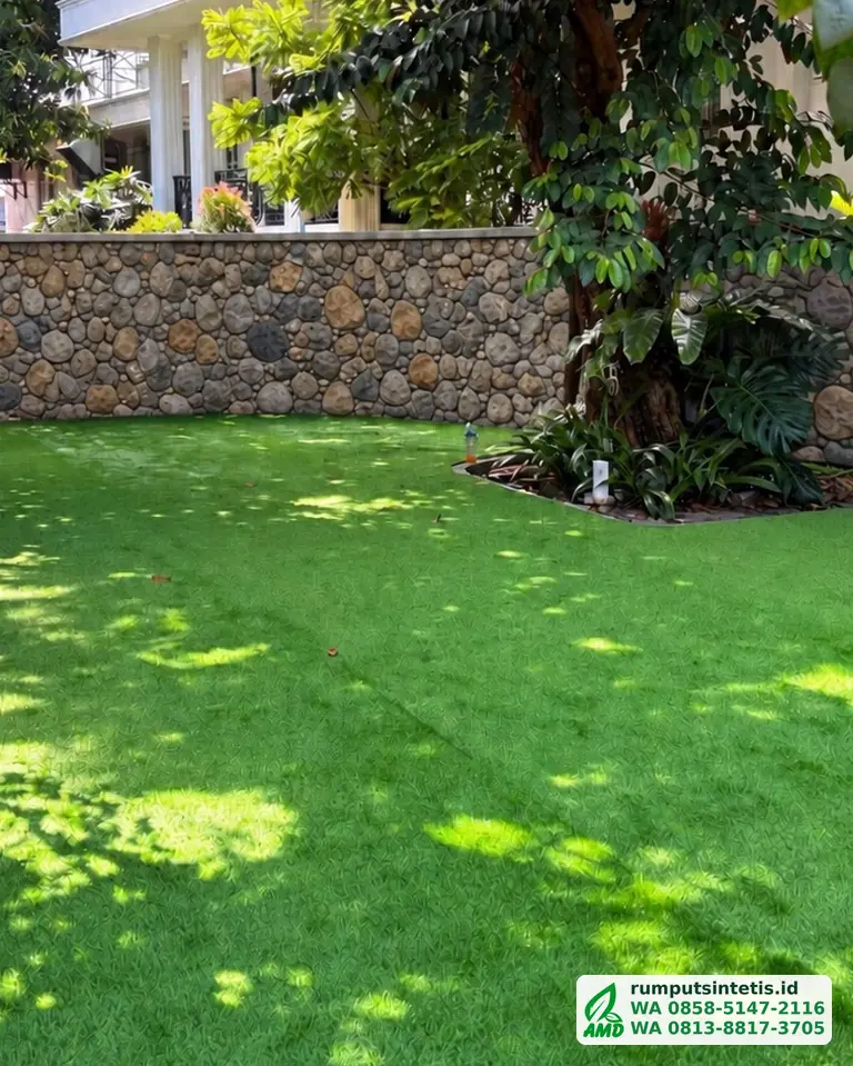 Taman rumput sintetis hijau di depan dinding batu