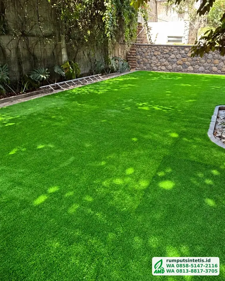 Taman rumput sintetis hijau di samping dinding batu